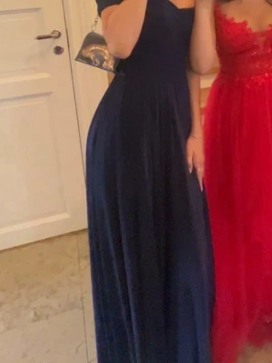 Marinblå balklänning  - Elegant marinblå långklänning med v-ringad hals, off shoulder. Klänningen har ett draperat liv och faller snyggt längs kroppen. Perfekt för bal eller festligare tillfällen. Materialet känns mjukt och följsamt.