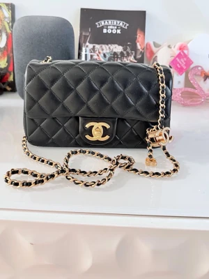 Svart quiltad axelväska i skinn - Säljer en ikonisk svart quiltad axelväska från i skinn med guldfärgade detaljer och klassisk kedjerem. Väskan har det välkända CC-spännet framtill och en elegant, tidlös design som passar till många olika stilar. Storlek 20cm i lambskinn