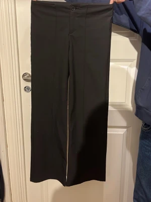 Svarta kostymbyxor med raka ben - Snygga svarta kostymbyxor med raka ben och klassisk passform. Byxorna har knapp och dragkedja framtill samt pressveck längs benen. Perfekta för en stilren look och enkla att matcha med olika överdelar.