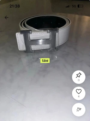 Vitt bälte med silverfärgat H-spänne - Snyggt vitt bälte med ett stort, blankt H-format spänne i silverfärg. Bältet har en stilren design och är tillverkat i slätt material som ger en clean look. Perfekt accessoar för att lyfta vilken outfit som helst.