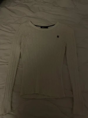 Vit kabelstickad tröja Gina Tricot - Kabelstickad vit tröja från Gina Tricot med rund halsringning och diskret broderad logga på bröstet. Tröjan har långa ärmar och ribbade muddar. Perfekt för lager på lager och enkel att matcha med olika stilar. Använd få tal gånger 