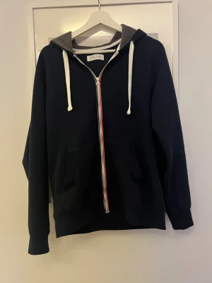  hoodie från pier one  - Snygg mörkblå hoodie från pier one med vit dragkedja och röda detaljer. Stor huva med grå insida och vita snören. Två stora fickor framtill och ribbade muddar. Perfekt för en chill och avslappnad stil.
