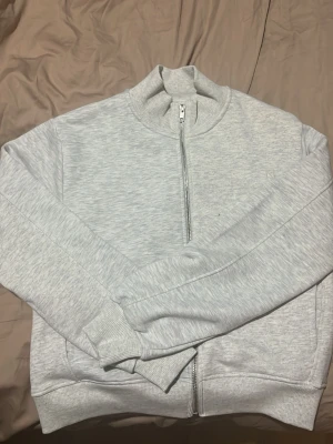 Ljusgrå ziptröja från Zara - Säljer en ljusgrå ziptröja från Zara med hög krage och hel dragkedja framtill. Tröjan har ribbade muddar vid ärmslut och nederkant, samt en mjuk bomullsblandning som gör den riktigt skön att bära. Perfekt till chill dagar eller när du vill ha en clean look.
