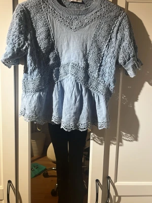 Blå spetsblus med volangdetaljer - Supersöt ljusblå blus med spetsdetaljer och volangkant. Blusen har korta ärmar och rund halsringning, samt vackra broderade partier som ger en romantisk känsla. Perfekt att styla med jeans eller kjol för en trendig look. Köpte på Zara för 55€ förra sommaren den är storlek S och är tajt kan se stor ut men den är tajt 