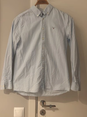  skjorta - Klassisk ljusblå skjorta från Gant med button-down krage och broderad logga på bröstet. Skjortan har långa ärmar och knäppning framtill. Perfekt för en stilren och avslappnad look. Den har en pytte liten svart prick men inget man tänker på. Kom dm för diskutera priset😄