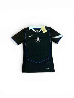 Chelsea FC 3rd kit 25/26 PLAYER VERSION  - Chelsea FC svart matchtröja från Nike med ljusblå detaljer och klubbmärke på bröstet. Nummer 10 och namnet Palmer på ryggen. Tröjan har korta ärmar och V-ringad krage med ljusblå inslag. Perfekt för fotbollsträning eller support.