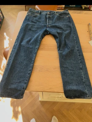 Levi's 501 blå jeans - Klassiska blå jeans från Levi's med rak passform och fem fickor. Jeansen har en mörkblå tvätt och är tillverkade i denim. Perfekta för en avslappnad och tidlös stil.