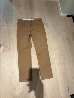 Bruna chinos från Mc Authentic - Snygga bruna chinos från Mc Authentic i modellen Slim. Klassisk rak passform med knapp och dragkedja i midjan. Tillverkade i ett mjukt bomullstyg som ger en skön känsla och stilren look. Perfekta för dig som gillar en enkel men trendig stil.