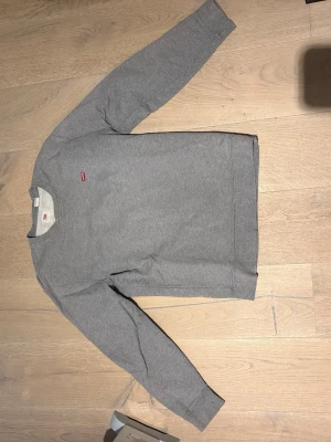 Grå sweatshirt från Levi's - Klassisk grå sweatshirt från Levi's med rund halsringning och liten röd logotyp på bröstet. Tröjan har långa ärmar och ribbade muddar vid ärmslut och nederkant. Tillverkad i mjukt bomullsmaterial för en skön och avslappnad look.