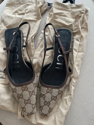 Gucci ballerinaskor med monogram - Snygga ballerinaskor från Gucci i beige canvas med brunt GG-monogram och bruna läderdetaljer. Skorna har fyrkantig tå och tunna remmar. Storlek 35,5 men dom är som storlek 36. Bra skick. Kvitto finns.