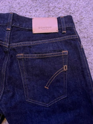 Mörkblå jeans från Dondup - Snygga mörkblå jeans från Dondup med klassisk femficksmodell och raka ben. Jeansen är tillverkade i denim och har en stilren look med kontrastsömmar. Perfekta för dig som gillar en clean och tidlös stil.