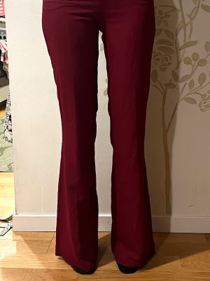 Vinröda utsvängda byxor -  Vinröda, tunna kostymbyxor med utsvängda ben och hög midja. Gott skick. 
