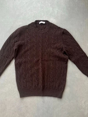 Brun kabelstickad tröja i ull/kashmir - Mysig brun kabelstickad tröja från Filippo De Laurentiis i en lyxig mix av ull och kashmir. Rund halsringning och ribbade muddar ger en klassisk look. Perfekt för dig som gillar stilrena och bekväma plagg.