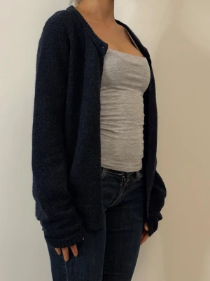 Mörkblå stickad kofta - Mysig mörkblå stickad kofta med lång ärm och avslappnad passform. Perfekt att slänga över en topp för en chill look. Koftan har enkel design utan knappar och är lätt att matcha med jeans eller kjol.