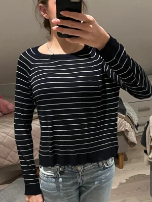 Svartvit randig långärmad tröja - Snygg svart långärmad tröja med tunna vita horisontella ränder. Tröjan har rund halsringning och ribbade muddar vid ärmslut och nederkant. Perfekt till jeans för en avslappnad stil.