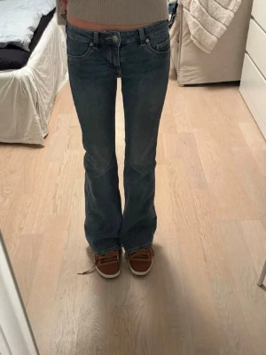 Blå bootcut jeans med låg midja - Snygga blå bootcut jeans med låg midja och klassiska fem fickor. Jeansen har en lätt tvättad look och sitter tajt upptill med utsvängda ben. Perfekta för en avslappnad och trendig stil.