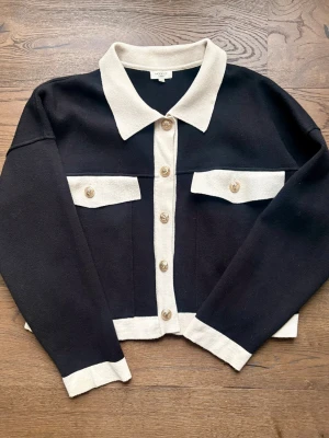 Svart och beige kofta från MOOCCI PARIS - Stilren svart kofta med beigea detaljer från MOOCCI PARIS, köpt på Raglady By Tara🖤Koftan är i ett väldigt fint och kvalitet material! Den har långa ärmar, beige krage, knäppning framtill med guldknappar och två fickor på bröstet. Ord pris: 800 kr Strl: S/M