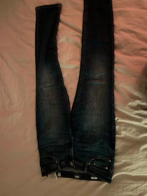 Mörkblå skinny jeans från Jack & Jones - Säljer ett par mörkblå slim glenn jeans från Jack & Jones med klassisk femficksdesign och snygga slitningar. Jeansen har en smal passform och är tillverkade i stretchigt denimtyg för extra komfort. Perfekta för en trendig och avslappnad look. Strl 12. 152cm