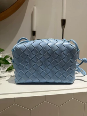 Ljusblå flätad axelväska i skinn - Supersöt ljusblå axelväska med flätad design och justerbar rem.  Köpt utomlands  men är i skin!! Passar perfekt för att piffa till outfiten och speciellt på sommarn💙använd en gång. Pris går att diskutera vid snabb affär!