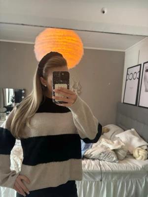 Beige och svart randig stickad tröja - Stickad tröja med breda beige och svarta ränder, hög hals och långa ärmar. Tröjan har en avslappnad passform och är perfekt för kalla dagar. Materialet ser ut att vara mjukt och mysigt, troligen akryl eller ullblandning.