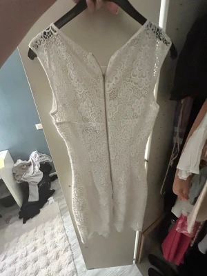 Vit spetsklänning med blommönster - Säljer en elegant vit kortklänning i spets med blommigt mönster. Klänningen är ärmlös, har rund halsringning och dragkedja i ryggen. Perfekt för sommarens alla tillfällen och ger en romantisk vibe.