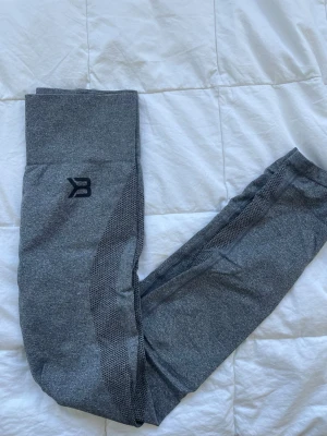 Grå sömlösa leggings från Better Bodies - Gråa sömlösa leggings från Better Bodies med hög midja och diskret logga på höften. Materialet är stretchigt och andas, perfekt för träning eller chill. Snygga mesh-detaljer längs sidorna ger extra stilpoäng.