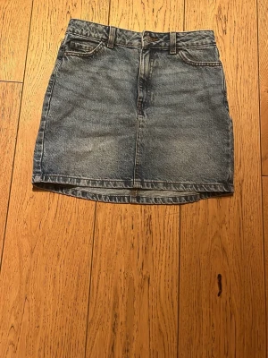 Blå jeanskjol i klassisk modell - Snygg blå jeanskjol i klassisk femficksmodell med bälteshällor och dragkedja fram. Kjolen är kort och har en rak passform, perfekt till sneakers eller boots. Tidlös denim som alltid funkar.