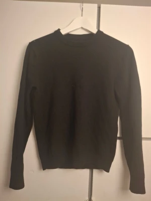 Svart tröja  - En enkel och stilren mörkgrå stickad tröja med rund halsringning och långa ärmar. Perfekt basplagg som passar till det mesta och har en klassisk passform. Tröjan är mjuk och skön, och funkar året runt.