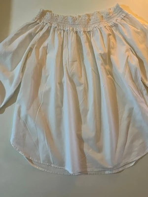 Vit offshoulder-blus från H&M - Snygg vit offshoulder-blus från H&M med smockad resår upptill. Blusen har en luftig passform och är tillverkad i ett lätt bomullstyg. Perfekt för en trendig och avslappnad look. Andvänd några gånger bara. Inga fläckar och ser helt ny ut. Det finns en blå/vit randig blus precis som denna också ( checka min profil). Storlek 34 och CN 160/80A. 