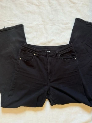 Svarta utsvängda jeans  - Säljer ett par svarta jeans med utsvängda ben och råa, avklippta benslut. Klassisk femficksmodell med hällor i midjan och dragkedja med knapp. Jeansen har en trendig och avslappnad vibe, perfekta till sneakers eller boots.
