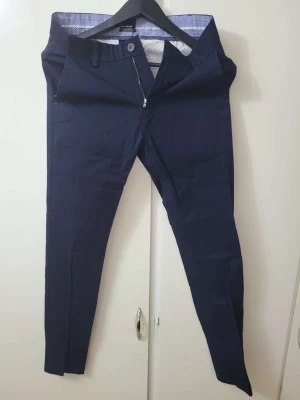 Mörkblå kostymbyxor från H&M - Snygga mörkblå kostymbyxor från H&M med smal passform och klassisk design. Byxorna har bälteshällor, knapp och dragkedja framtill samt två sidofickor. Perfekta för en stilren look.