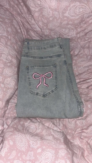 Ljusblåa jeans med rosetter - Ljusa jeans med broderade rosetter på bakfickorna, har en utsvängd passform. Endast testade och dom passade mig inte, för korta i benen men midjan satt bra. Är 1,70cm så skulle säga att nån 1,65cm skulle passa bra i dom. Strl 36/S.