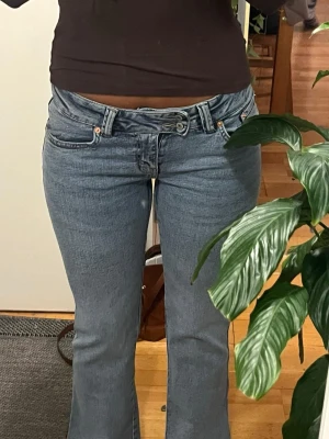 Blåa jeans  - HELT NYA!!!!! Säljer ett par ljusblå bootcut jeans med låg midja och klassisk femficksdesign. Jeansen har en unik asymmetrisk knäppning framtill och är tillverkade i denim. Perfekta för dig som gillar en trendig och avslappnad stil.