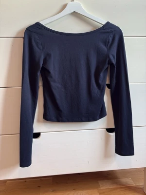Marinblå  långärmad croppad topp - En stilren marinblå långärmad topp med croppad passform och bred, rundad där bak i ryggen. Tillverkad i mjukt bomullsmaterial som sitter skönt mot kroppen. Perfekt att matcha med jeans eller kjol för en trendig look.