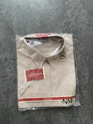 Beige skjorta från Noble Man - Stilren beige skjorta från Noble Man, perfekt för dig som gillar en klassisk look. Skjortan har knappar framtill och är långärmad. Passar till många olika outfits och är tillverkad i ett mjukt material som känns skönt mot huden.