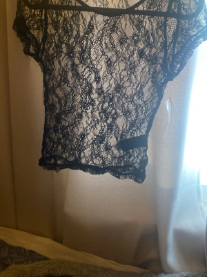Svart spetsig croppad topp - Snygg svart croppad topp i spets med korta ärmar och transparent design. Perfekt för att skapa en edgy look. Toppens spetsmönster ger en cool och trendig vibe.