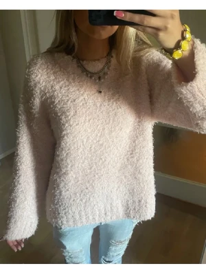 Ljusrosa fluffig stickad tröja - Supermjuk och fluffig stickad tröja i ljusrosa färg. Tröjan har rund halsringning, långa ärmar och ribbade muddar vid ärmslut och nederkant. Perfekt för dig som gillar en cozy och chill vibe.