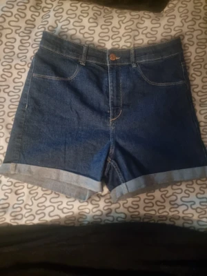 Mörkblå denimshorts med uppvik - Snygga mörkblå jeansshorts med klassisk femficksdesign och uppvikta benslut. De har hög midja och är gjorda i bomull för en skön och avslappnad känsla. Perfekta för sommardagar och enkel att matcha med allt.