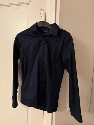 Mörkblå skjorta Tiger of Sweden - Snygg mörkblå skjorta från Tiger of Sweden i extra slim fit. Skjortan har klassisk krage, långa ärmar och knappar framtill. Perfekt för dig som gillar en stilren och tajt look.