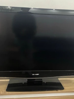 Sharp TV - Sharp platt-TV med bred skärm, klassisk svart design och stabil fot. Skärmen ser ut att vara i gott skick utan synliga repor eller skador. Perfekt för vardagsrummet eller sovrummet. Inga synliga defekter eller större slitage på ramen.