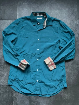 Burberry skjorta turkos - Burberry skjorta turkos i bra skick, inga tecken på slitage, använd en del. Endast skjortan ingår.