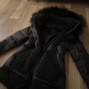 Svart dunjacka från rockandblue - Dunjacka från Rockandblue. Den är knappt använd. Den är praktisk på så sätt att den har många fickor och en justerbar midja. Det är en fuskpäls på jackan. Ny pris 4300kr säljer denna för 800kr. Peeler jacka nu inför vintern. 