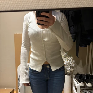 Vit ribbad kofta från Bik Bok - Säljer en fräsch vit ribbad kofta från Bik Bok i storlek XS. Tröjan har v-ringad hals, långa ärmar och är tillverkad i mjukt stickat material. Den har en slim passform och knäppning framtill. Perfekt att styla med jeans eller kjol för en clean look. Helt ny!
