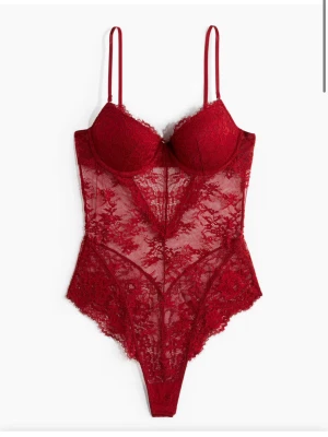 Röd spetsbody med smala axelband - Säljer en djup röd body med tunna axelband och vacker spetsdesign. Body har en figurnära passform och är genombruten med blommigt spetsmönster. Perfekt för dig som vill ha något extra snyggt och unikt i garderoben.