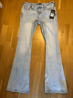 True Religion Joey Flare Jeans ljusblå - Ljusblå flare jeans från True Religion, modell Joey. Snygga broderade bakfickor med lock och silverknappar. Klassisk femficksmodell i tvättad jeans med bootcut och hög midja. Perfekta för dig som vill ha en retrovibe och statement-detaljer.