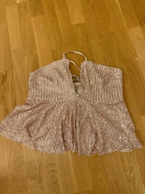 Glittrig ljusrosa paljett tubtopp - Säljer en glittrig ljusrosa topp med paljetter och bandeau-form. Toppen har snörning i ryggen har ett lätt utsvängt fall nedtill. Perfekt för att sticka ut med extra bling och snygg passform.