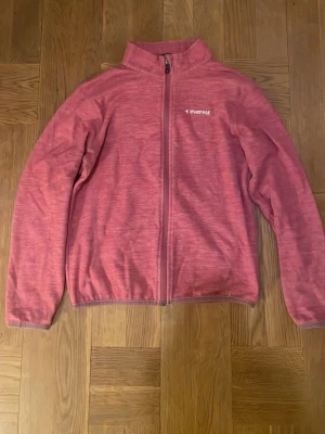 Rosa fleecejacka från Everest - Säljer en rosa fleecejacka från Everest med hel dragkedja framtill och ståkrage. Jackan har långärmade ärmar och är tillverkad i mjuk fleece som är perfekt för kyliga dagar. Diskret logga på bröstet och enkel design som funkar till många stilar. Dragkedjan är lite trög men funkar helt annars. Flisen är rätt så gammal och passar inte längre så det är därför jag säljer den. Pris kan diskuteras och om du har någon fråga så är det bara att ställa!
