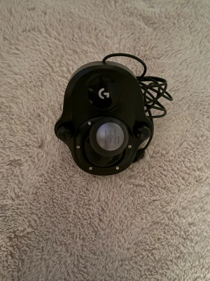 Logitech Driving Force Shifter - Logitech Driving Force Shifter till racingspel, kompatibel med G29 och G920 rattar. 6-växlad manuell växelspak med solid konstruktion. Kabel och fäste ingår. Produkten ser ut att vara i gott skick utan synligt slitage eller defekter.