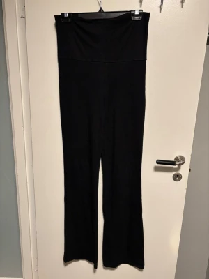 Svarta höga mjukisbyxor wide - Svarta mjukisbyxor med hög midja och wide fit. Byxorna har en enkel design utan synliga detaljer och är gjorda i ett mjukt material som känns skönt mot huden. Perfekta för chill dagar eller när du vill ha något bekvämt och stilrent.