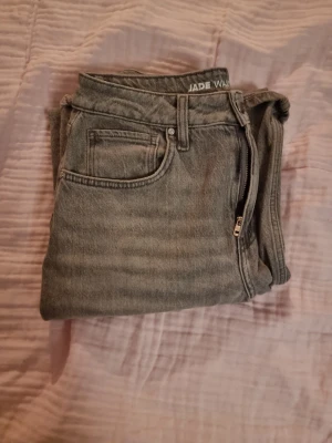 Gråa wide jeans från Gina Tricot - Säljer ett par gråa jeans från Gina Tricot med hög midja och raka, breda ben. Modellen heter Jade och har klassisk femficksdesign, dragkedja och knapp framtill. Jeansen är tillverkade i jeansmaterial och har en cool, lite tvättad look.